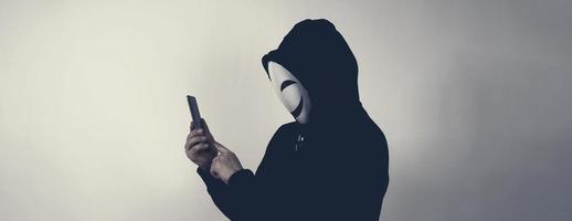 hacker anónimo y mascarilla con smartphone en la mano. foto