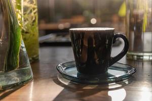 coffee latte art cup in coffee shop. hot Coffee in black mug on wooden table in cafe with plant in glass vase and sunlight background photo