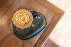 top view of coffee latte cup in coffee shop. hot macchiato coffee with caramel arts in black mug on wooden table in cafe with copy space and sunlight background photo