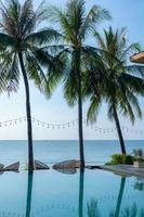 Beautiful tropical beach and sea with palm tree, coconut tree and chair around swimming pool in hotel resort for travel and vacation. relaxing summer in infinity swimming pool looking at view. photo