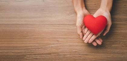 mano de mujer con corazón rojo sobre fondo de madera, atención médica, amor, donación de órganos, seguro familiar, csr, día mundial del corazón, día mundial de la salud, concepto de oración, vista superior. foto