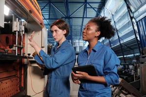 Two professional female engineer workers in safety uniforms work by inspecting machines' voltage current, checking, and maintaining at manufacturing factory, electric system service occupations. photo