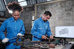 Two professional industry engineer workers partner in safety uniforms metalwork jobs with mechanical drawing in a monitor, lathe machines tools, and production part workshop in manufacturing factory.