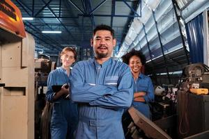 Multiracial industry workers in safety uniforms collaborate with unity, arms crossed, and express happy work together with smile and cheerful in mechanical factory, professional engineer occupation. photo