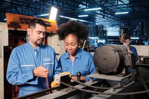 Asian male and female African American engineers in safety uniform work by inspecting machines' voltage current, checking, and maintaining at manufacture factory, electric system service occupations. photo