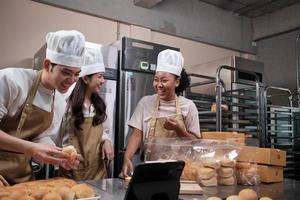 tres jóvenes socios de inicio de chefs, blogger de pequeñas empresas que transmiten en vivo a través de tecnología de aplicaciones móviles, promoción de ventas de panadería en línea, pan fresco, comida de pastelería y cocina comercial. foto