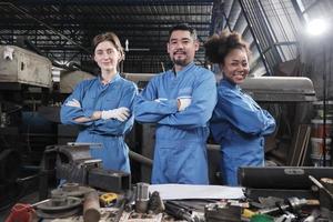 Multiracial industry workers in safety uniforms collaborate with unity, arms crossed, and express happy work together with smile and cheerful in mechanical factory, professional engineer occupation. photo