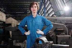 Portrait of one young Caucasian female industry worker in safety uniform stand, looking at camera and akimbo and expresses solemn confidence in a mechanical factory. Professional engineer occupation. photo