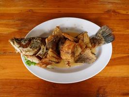 pescado pargo frito cubierto con salsa de pescado en un plato blanco sobre una mesa de madera foto