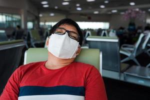 hombre asiático obeso con mascarilla protectora sentado durmiendo en el asiento del aeropuerto foto