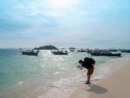 Asian backpacker tourist man taking photograph of sea wave with smartphone at sunny beach with sunlight reflection on water surface on Lipe island photo