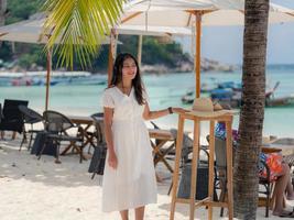 mujer asiática vestida de blanco parada cerca de un paraguas en un café al aire libre junto al mar disfruta mirando la hermosa vista foto