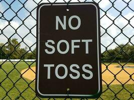 black no soft toss sign on metal fence at baseball field