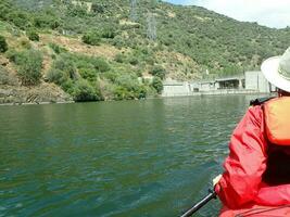 kayakista en chaleco naranja con sombrero en kayak en río con colinas foto