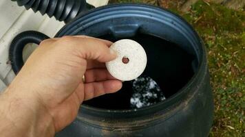 mano que sostiene el insecticida de la tableta del mosquito sobre el barril de lluvia foto