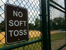 black no soft toss sign on metal fence at baseball field photo