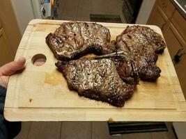 hand holding cutting board with grilled beef steaks in kitchen photo