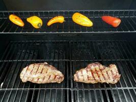 steaks on barbecue grill with colorful peppers photo