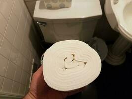 hand holding toilet paper roll without center over toilet photo