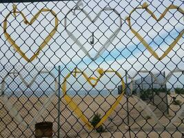 Corazones de bolsas de plástico amarillas y blancas en una cerca de eslabón de cadena de metal en la playa foto