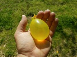 hand holding yellow water balloon over green grass photo