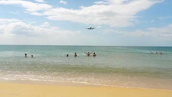 gente en la playa de mai khao nadando en el mar y viendo el aterrizaje del avión en el aeropuerto de phuket.