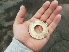 hand holding circular metal disk and black asphalt photo