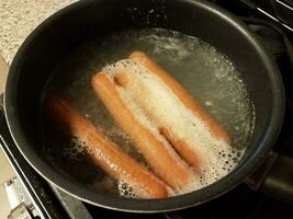 hot dogs boiling in water in pan on stove photo
