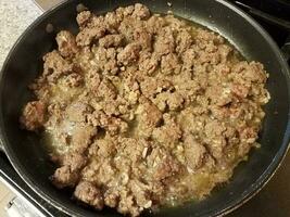 Carne molida cocinando en sartén en estufa con ajo foto