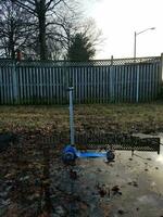 scooter azul en charco de agua y valla de madera foto