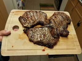 hand holding cutting board with grilled beef steaks in kitchen photo