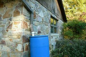 blue rain barrel with downspout and stone building photo