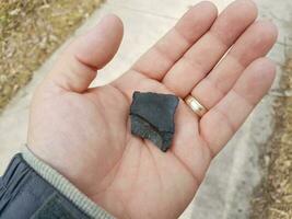 hand holding black burnt piece of wood over cement photo