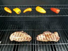 steaks on barbecue grill with colorful peppers photo