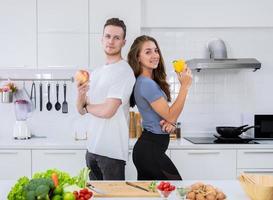 pareja amante feliz cocinando juntos en la cocina. joven y mujer de pie y sosteniendo frutas y verduras frescas en sus manos foto