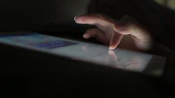 le doigt d'une femme glisse sur l'écran d'une tablette pour lire les médias sociaux sans allumer la lumière, au lit avant de s'endormir. video