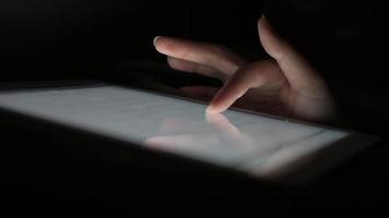 el dedo de una mujer se desliza sobre la pantalla de una tableta para reproducir las redes sociales sin encender la luz, en la cama antes de quedarse dormida. video