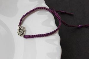 purple braded bracelet with chakra sahasrara on the edge of a snow-white plate photo