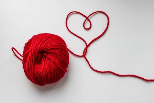 Ball of red yarn with a heart-shaped thread on white background photo