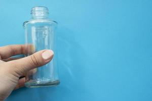 Transparent glass empty bottle in hand on a blue background with place for your design. photo