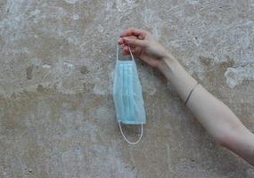 A used medical mask in the hand of a young woman against the background of a concrete wall on the street. Conceptual photo