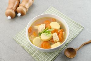 Clear soup with egg tofu, carrot and shrimp meatballs. Served in white bowl on grey background. photo