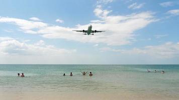 gente en la playa de mai khao nadando en el mar y viendo el aterrizaje del avión en el aeropuerto de phuket. video