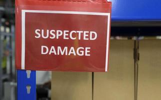 A shelf with packages and a sign saying SUSPECTED DAMAGE photo