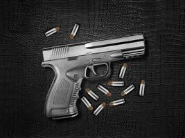 pistola de metal plateado y balas sobre un fondo de cuero negro foto