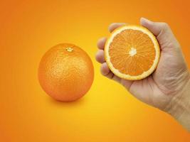 mano sosteniendo frutas naranjas y rodajas de naranja sobre fondo naranja foto