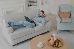 Young businessman working remotely at home while lying on couch photo