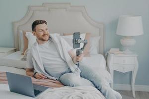 Young man lying  on bed while video chatting using phone photo