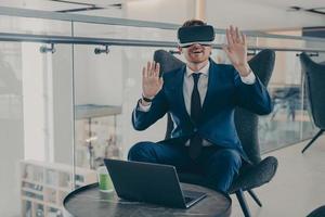 Businessman in formal suit and in VR headset glasses pointing with open palms up in air photo