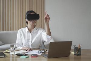 Female office worker in vr headset interacting with digital interface, touching 3d objects photo